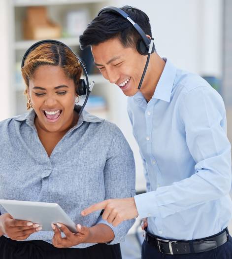 Two happy young diverse call centre telemarketing agents working on a digital tablet in an office. .